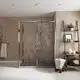 Duschbereich mit Glasabtrennung und Handbrause von Ideal Standard. Offene Regale zeigen Badezimmeraccessoires. Rustikale Wand mit freiliegendem Mauerwerk und neutralem Bodenbelag.